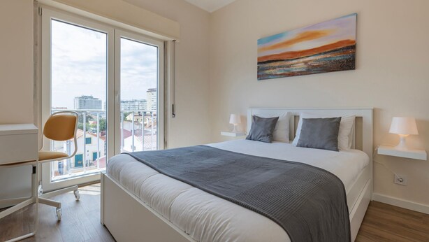 Ein Hotelzimmer mit einem großen Bett, einem Sessel, einem Schreibtisch und einem Fenster mit Blick auf die Stadt.