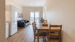 Ein kompakter Wohnbereich mit Küchenzeile, einer Essecke mit Holztisch und -stühlen, einer Couch und einem großen Fenster mit Blick auf die Stadt.