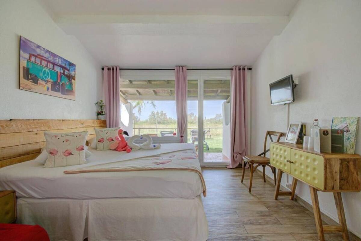 A bedroom with a bed, a wooden dresser, a television, and a balcony with curtains.