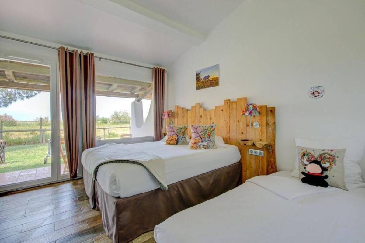 A bedroom with two beds, a wooden headboard, and a large window with curtains.