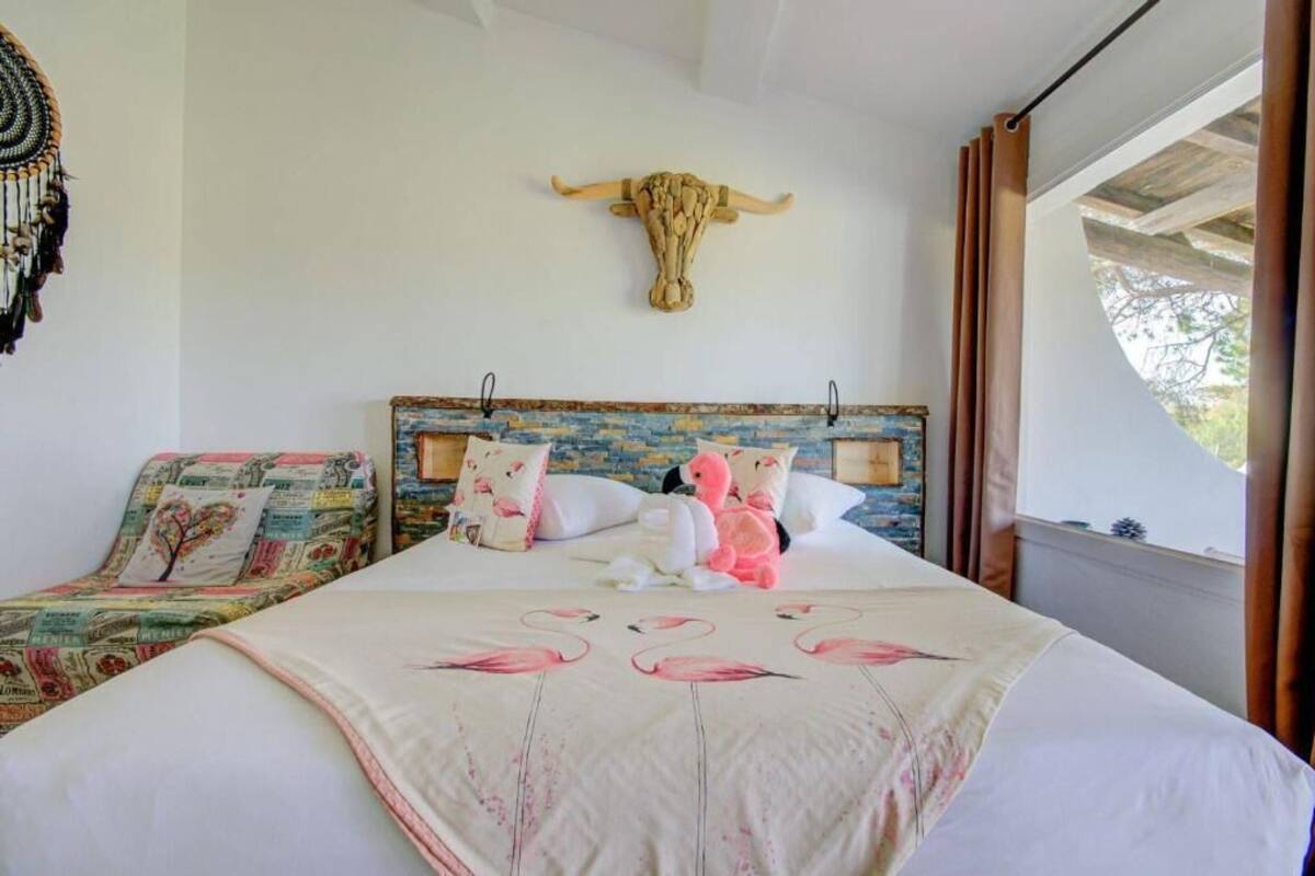 A bedroom with a bed featuring a white and pink flamingo print bedspread, a rustic headboard, and a decorative bull head on the wall.