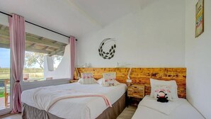Ein Schlafzimmer mit zwei Betten, einem Holz-Kopfteil, einer Wandleuchte und einem Fenster mit Vorhängen.