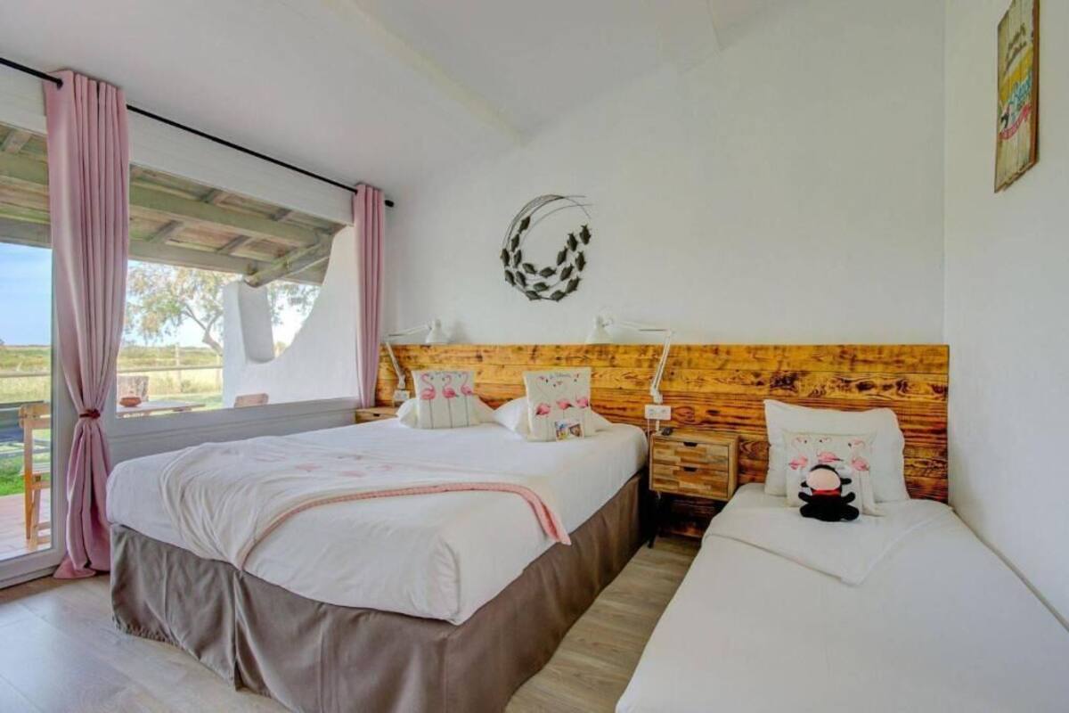 A bedroom with two beds, a wooden headboard, a wall-mounted light, and a window with curtains.