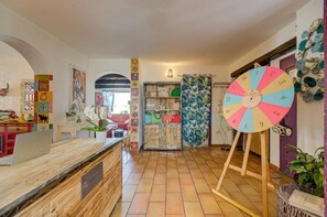 Un espace d’accueil avec un bureau en bois, une roue à filer aux couleurs vives et une plante.