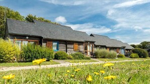 A row of wooden cottages with sloped roofs, surrounded by lush greenery and a clear sky.