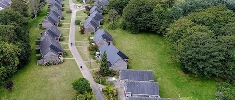 An aerial view of a residential area with houses arranged in rows, a central pathway, and surrounding greenery.