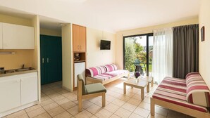 A compact living space with a kitchenette, a sofa, a dining table, and a sliding glass door to a garden.
