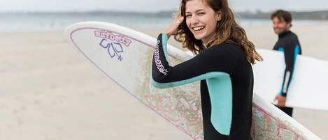 A person in a black and teal wetsuit holding a surfboard with stickers on it.