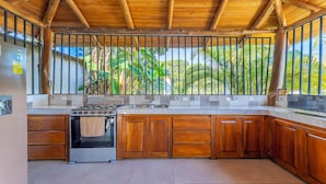 Una cocina con armarios de madera, una estufa y vista a vegetación exuberante.