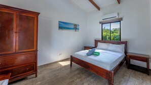 Un dormitorio con cama de madera, mesita de noche, cómoda y ventana con vistas a follaje.
