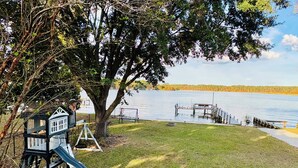 A playground with a slide and swings, a tree, and a lake with docks. - Family friendly lakefront home with private boat ramp and dock (Summerton)