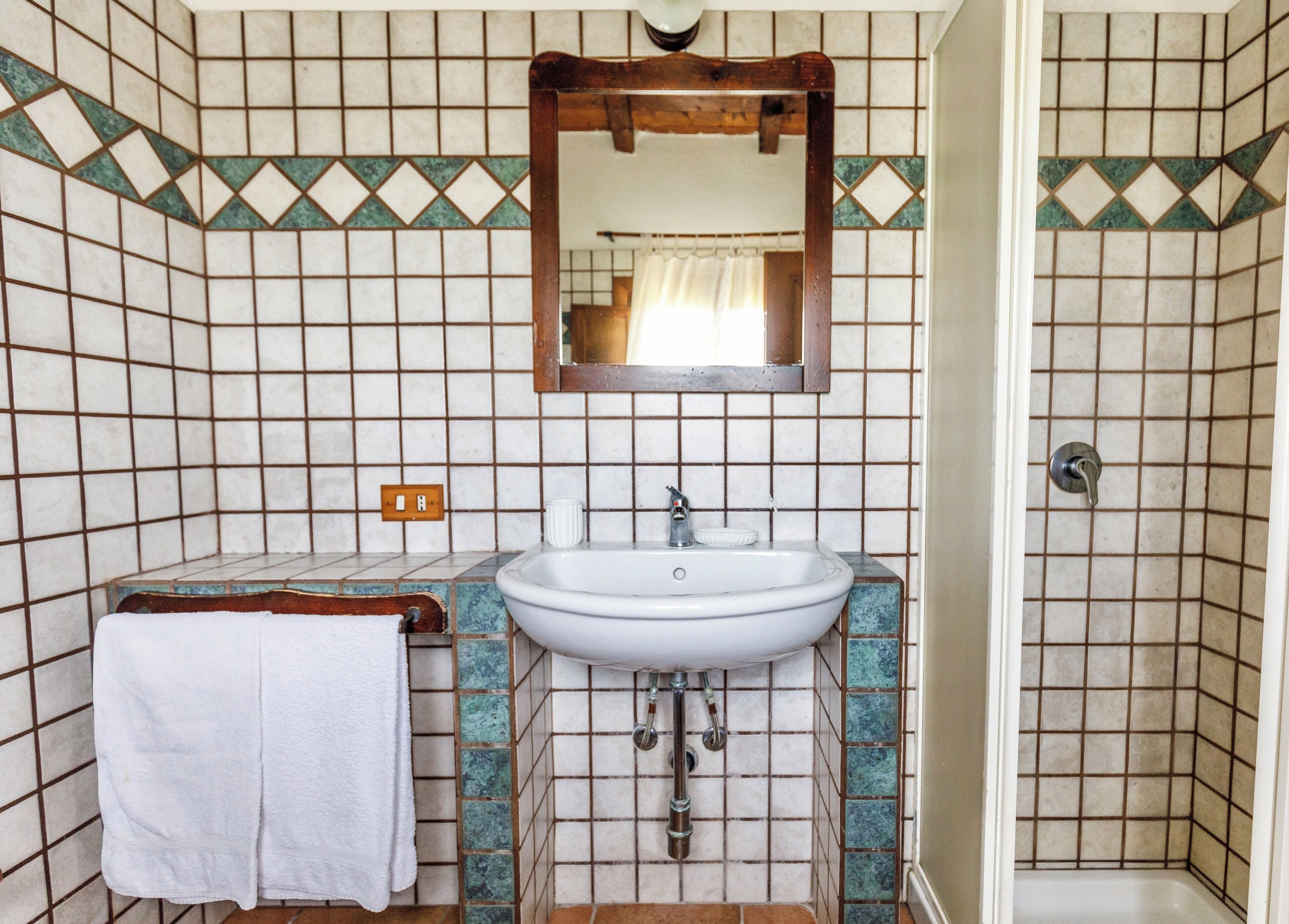 Ein Badezimmer mit einem weißen Waschbecken, einem Spiegel darüber und einer Duschkabine.