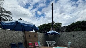 Een rechthoekig zwembad met een houten terras, omringd door ligbedden en parasols.