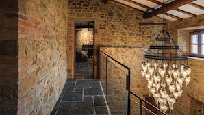 A stone-walled hallway with a chandelier, wooden beams, and a fireplace in the background. - La Tuscia - Tenuta di Toscana Boutique Villa (Gaiole in Chianti)