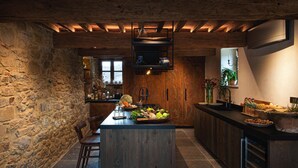 A rustic kitchen with a central island, stone walls, wooden beams, and a variety of food items displayed. - La Tuscia - Tenuta di Toscana Boutique Villa (Gaiole in Chianti)
