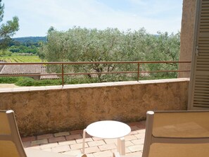 Ein Balkon mit Tisch und Stühlen, mit Blick auf einen Weinberg und Bäume.