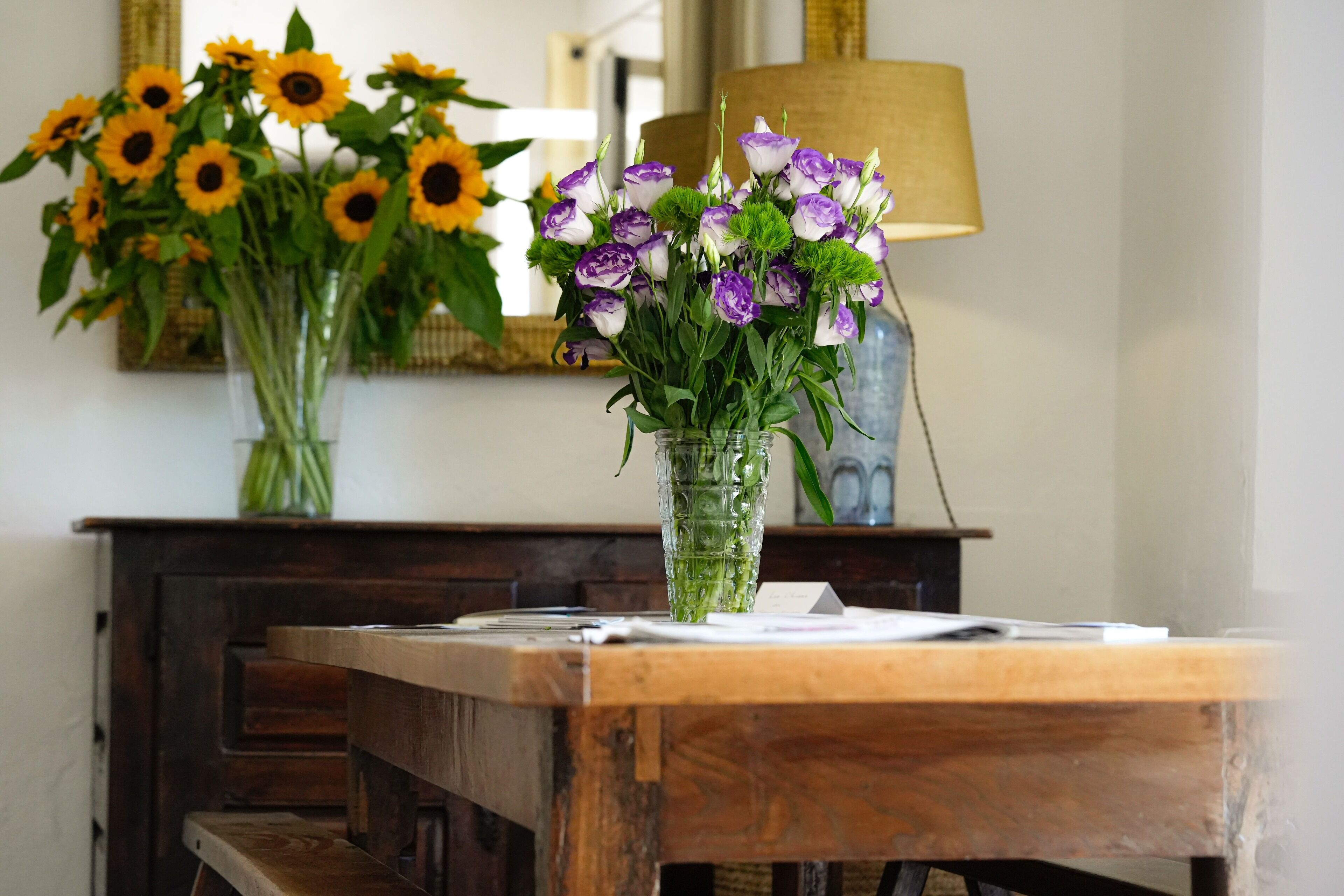 Une table en bois ornée d’un vase contenant des fleurs violettes et blanches, et d’un autre vase avec des tournesols.