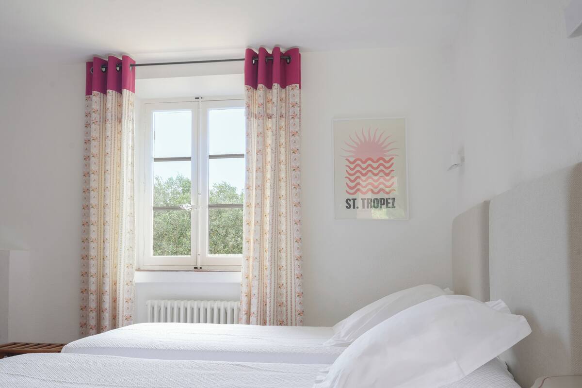 Une chambre à coucher avec un lit, une fenêtre avec des rideaux, un radiateur et un tableau encadré au mur.
