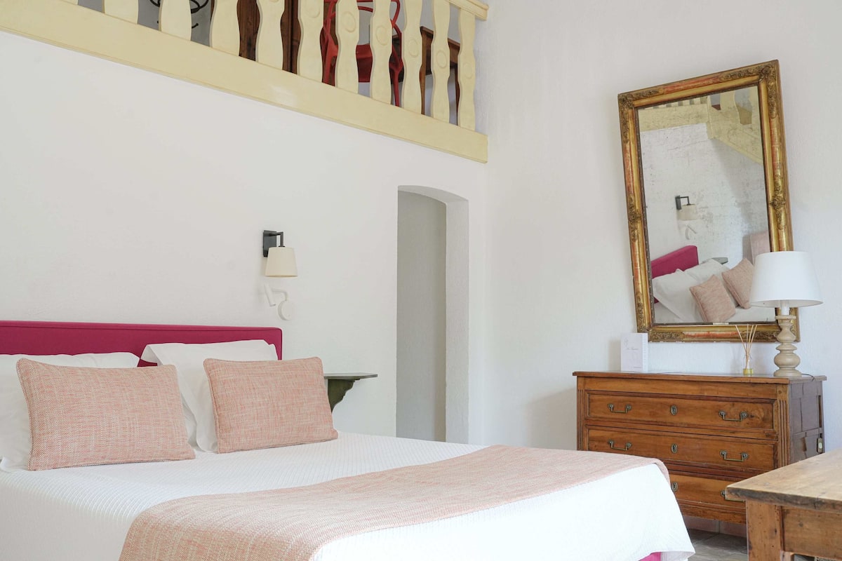 Une chambre à coucher bien rangée, avec un lit, une commode, un miroir et une lampe.