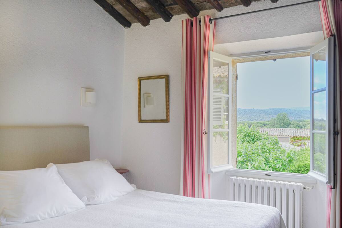 Une chambre à coucher avec un lit, une fenêtre avec des rideaux, un radiateur et un tableau encadré au mur.