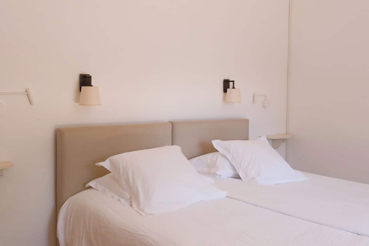 Un lit bien fait, avec du linge de lit blanc, deux lampes fixées au mur et une simple tête de lit.