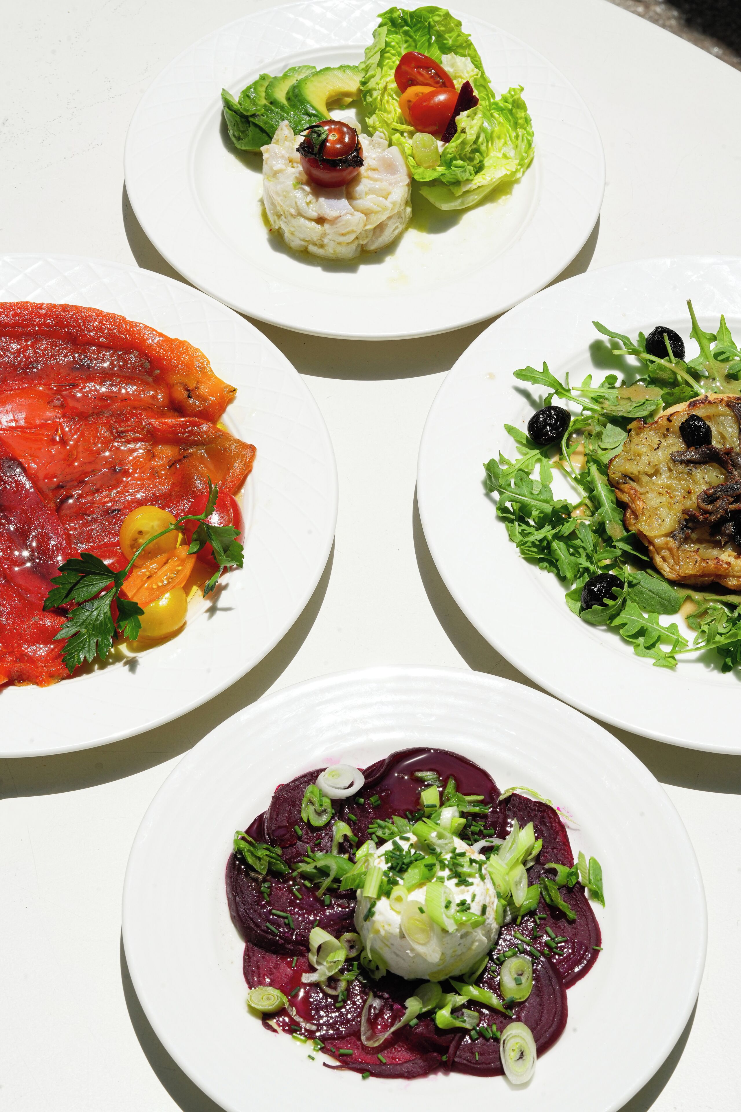 Four plates of food with various vegetables and garnishes.
