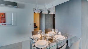 Un espace de salle à manger moderne avec une table en verre, des chaises en métal et des luminaires suspendus.