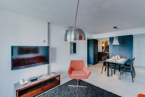 Un salon moderne avec un téléviseur à écran plat, un fauteuil rouge, une table à manger avec des chaises et un tapis noir.