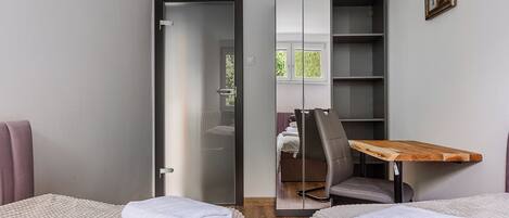 Habitación de hotel con dos camas, una mesa de madera, una silla, un armario y una ventana.