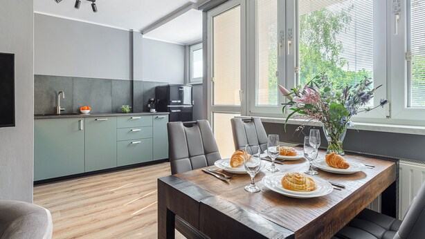 Une cuisine moderne avec des meubles gris, une table à manger dressée avec des assiettes, des verres et un vase de fleurs.
