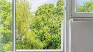 Une fenêtre donnant sur une végétation luxuriante et, au loin, sur un bâtiment.