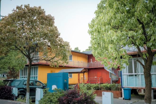 A residential building with a yellow exterior, a blue utility box, and a staircase leading to a balcony.