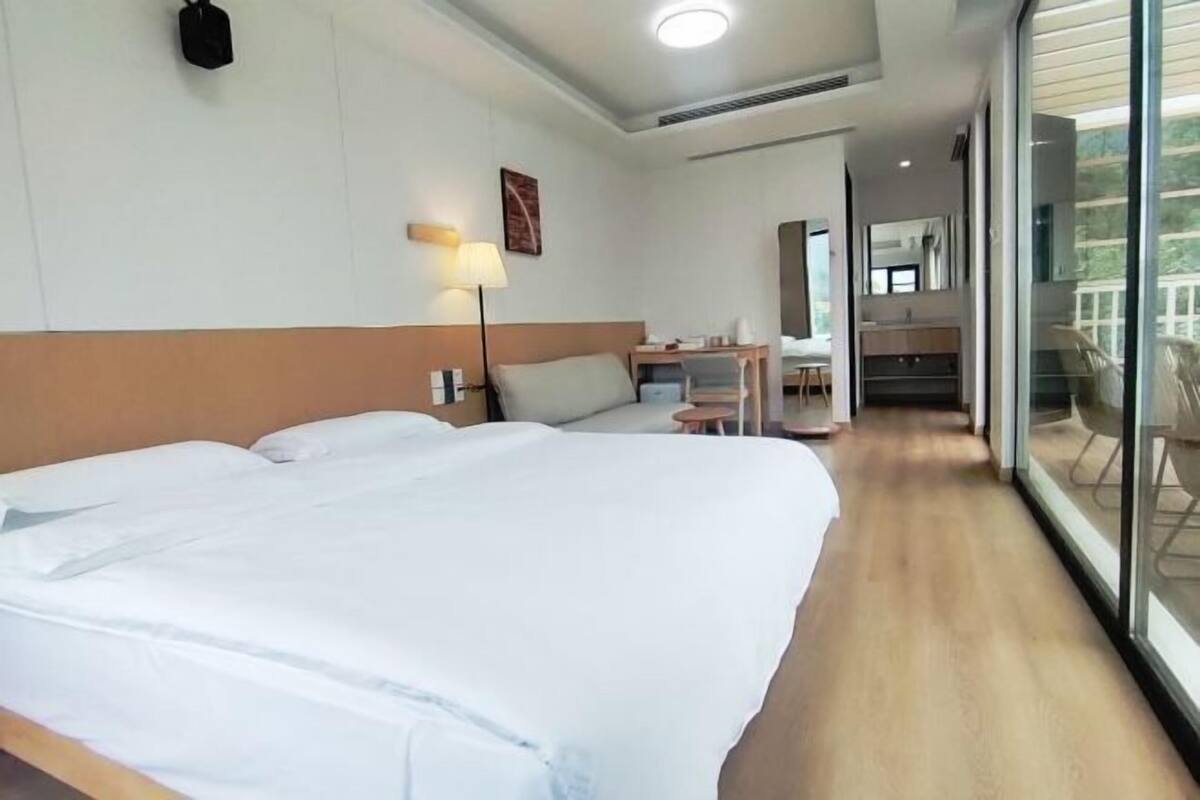 Une chambre d’hôtel avec un grand lit, un bureau, une chaise, une lampe et une vue sur l’extérieur grâce à une porte vitrée.
