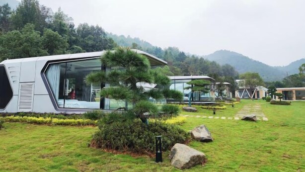 A modern, eco-friendly resort with sleek, contemporary architecture, featuring large glass windows and a well-maintained garden with a prominent bonsai tree.