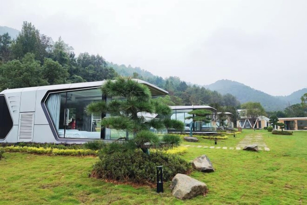 A modern, eco-friendly resort with sleek, contemporary architecture, featuring large glass windows and a well-maintained garden with a prominent bonsai tree.