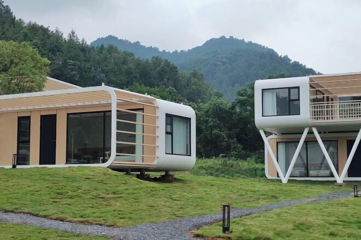 Two modern, curved buildings with large windows, set against a mountainous backdrop.