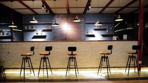 A bar area with five stools, wooden shelves with bottles, and pendant lighting.