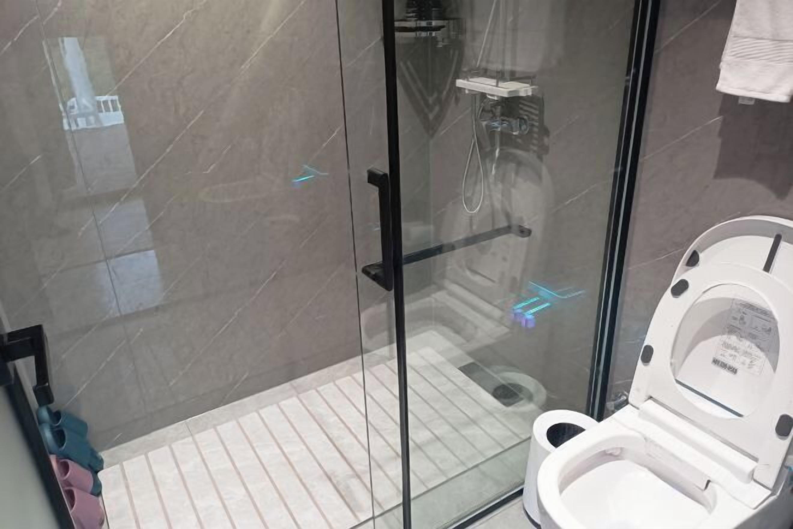 A modern bathroom with a glass shower enclosure, a white toilet, and a tiled floor.