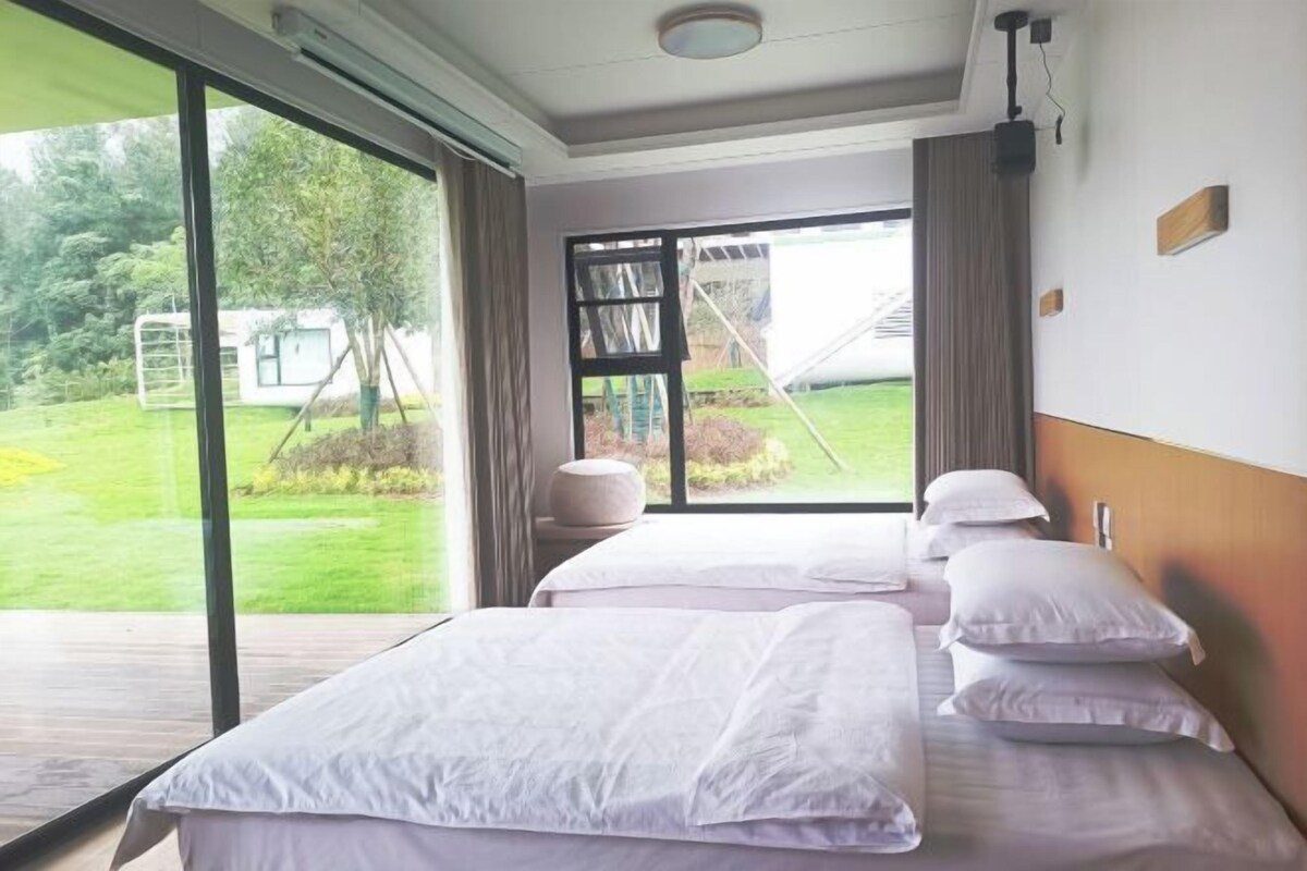 A hotel room with a large sliding glass door leading to a garden, a bed with white linens, and a wooden headboard.
