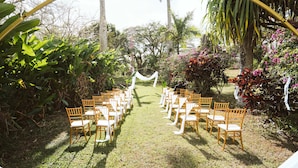Location all'aperto per un matrimonio, con file di sedie di legno e un arco bianco.