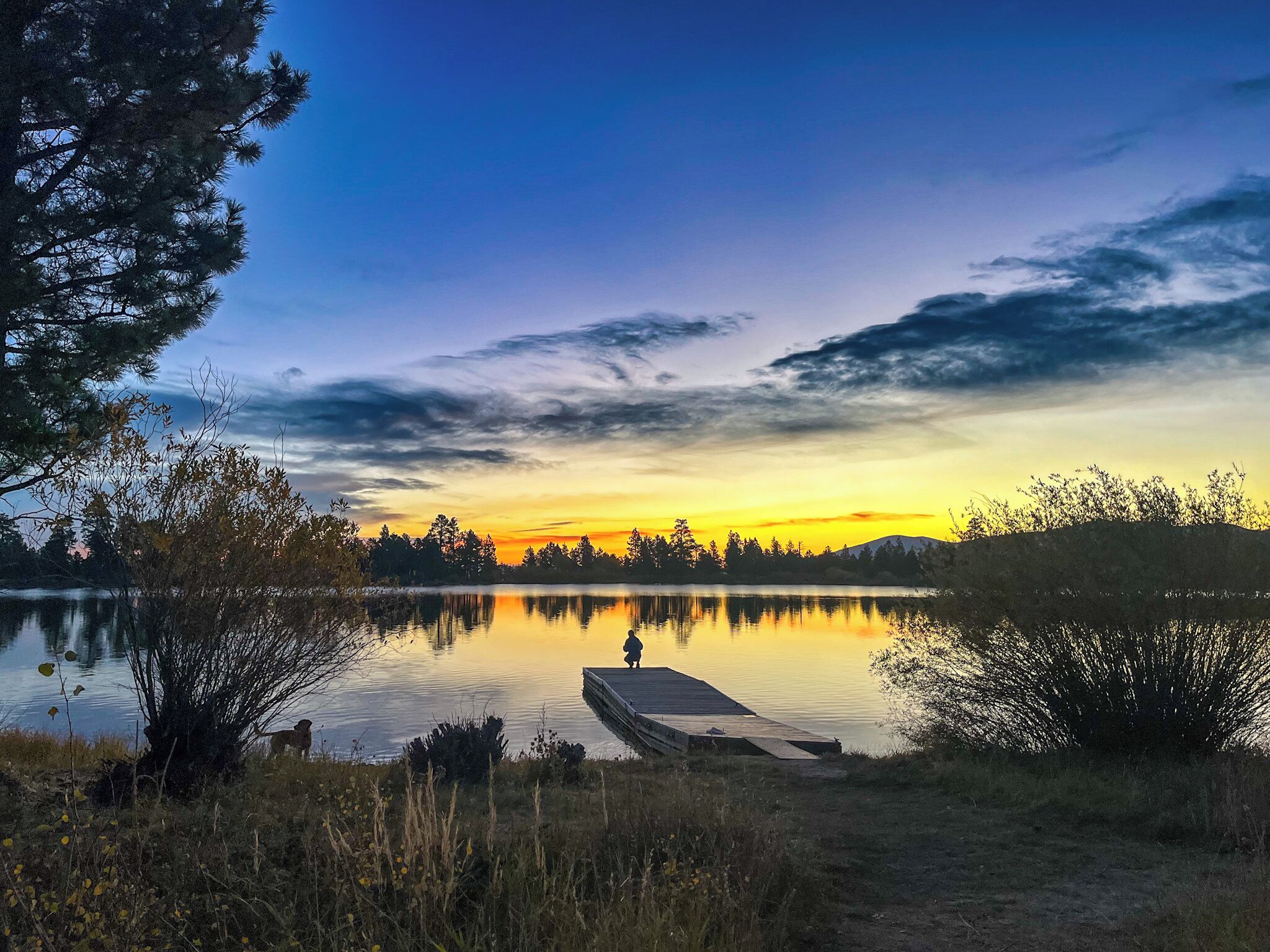 A calm lake at sunset with a wooden dock extending into the water.