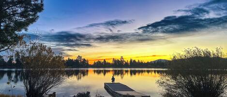 A calm lake at sunset with a wooden dock extending into the water.