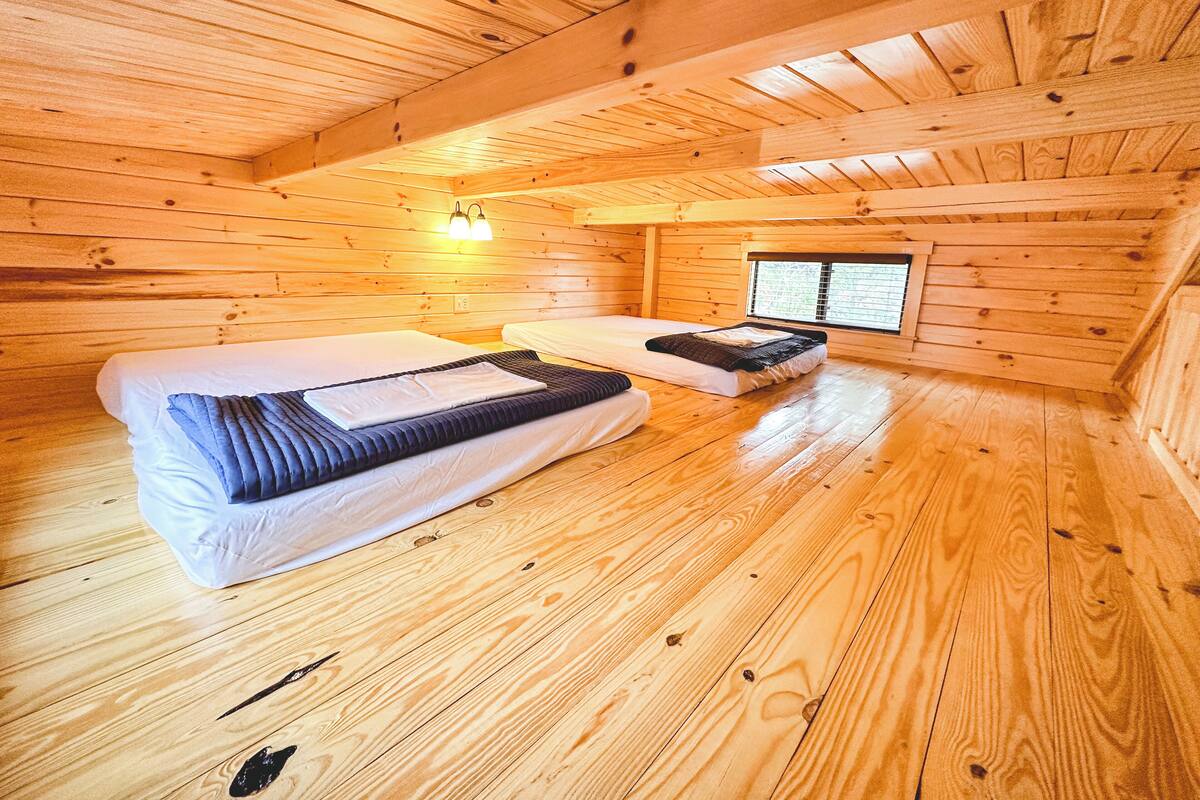 A wooden cabin room with two beds, a window, and a wall-mounted light fixture.