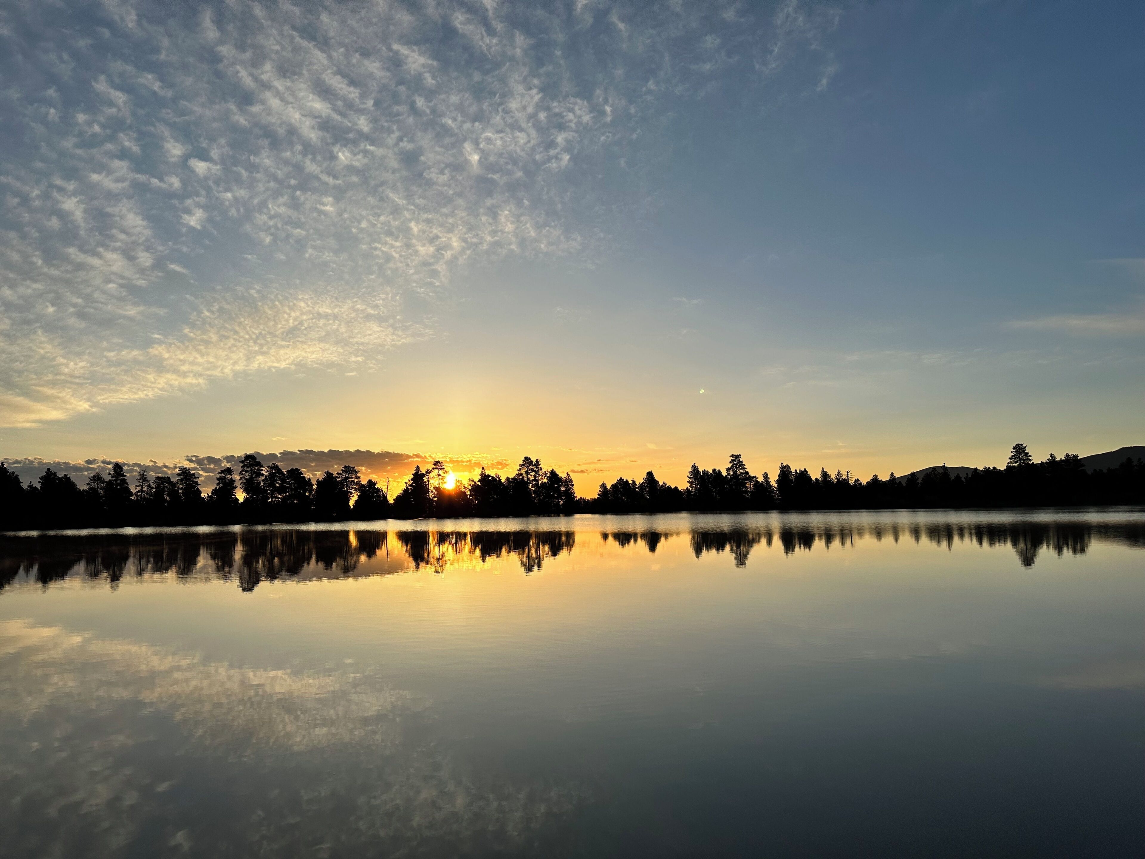 A calm lake reflecting the sky and trees at sunset.