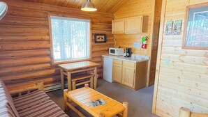 A cozy cabin interior with a wooden dining table, a sofa, a small kitchen area with a microwave, and a window providing natural light. - Red Canyon Lodge (Dutch John)