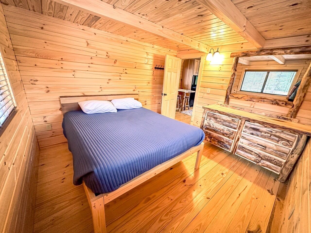 A wooden cabin bedroom with a bed, a dresser, and a window.