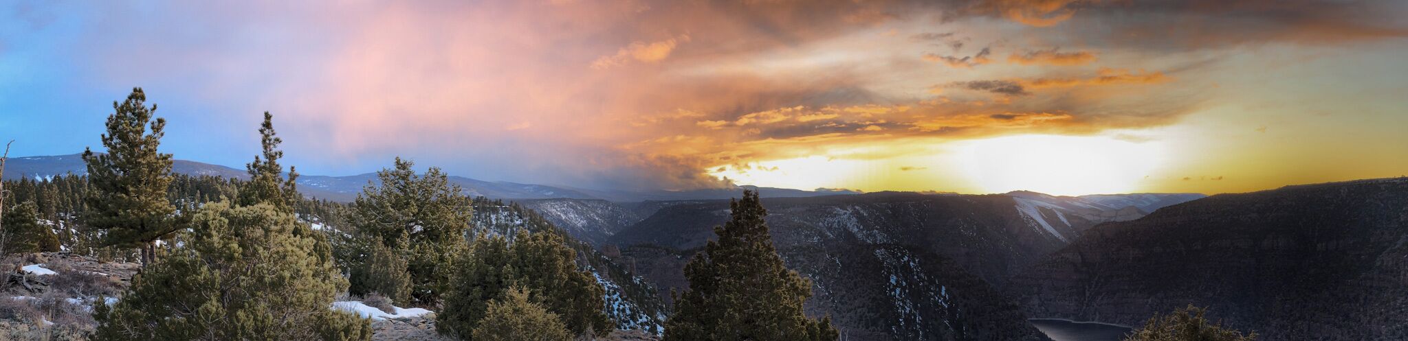 Paisaje montañoso con árboles cubiertos de nieve y un atardecer.