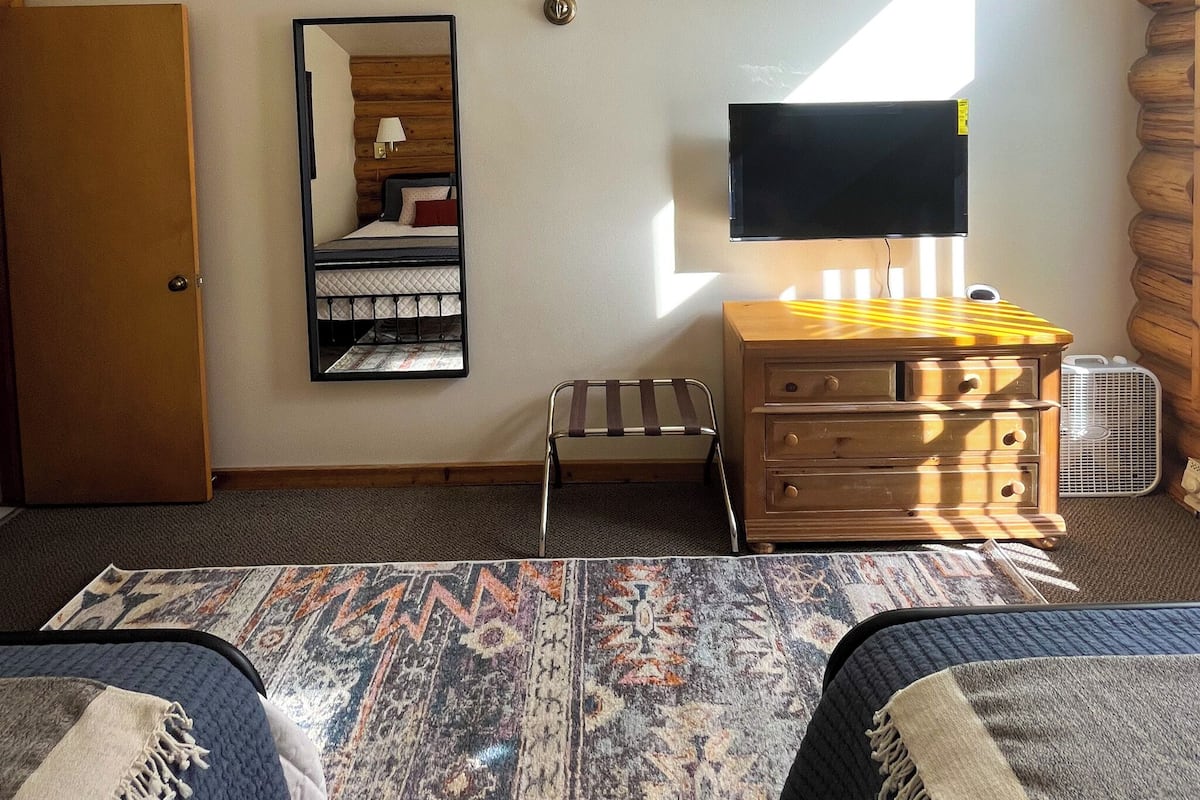A bedroom with a bed, a dresser, a mirror, a television, and a fan.