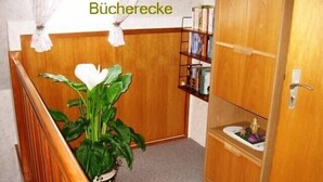 A hallway with a wooden staircase, a potted plant, a bookshelf, and a door labeled "Büchercke".