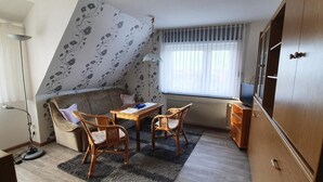 A cozy room with a sofa, two chairs, a small table, a radiator, a window with curtains, and a wardrobe.